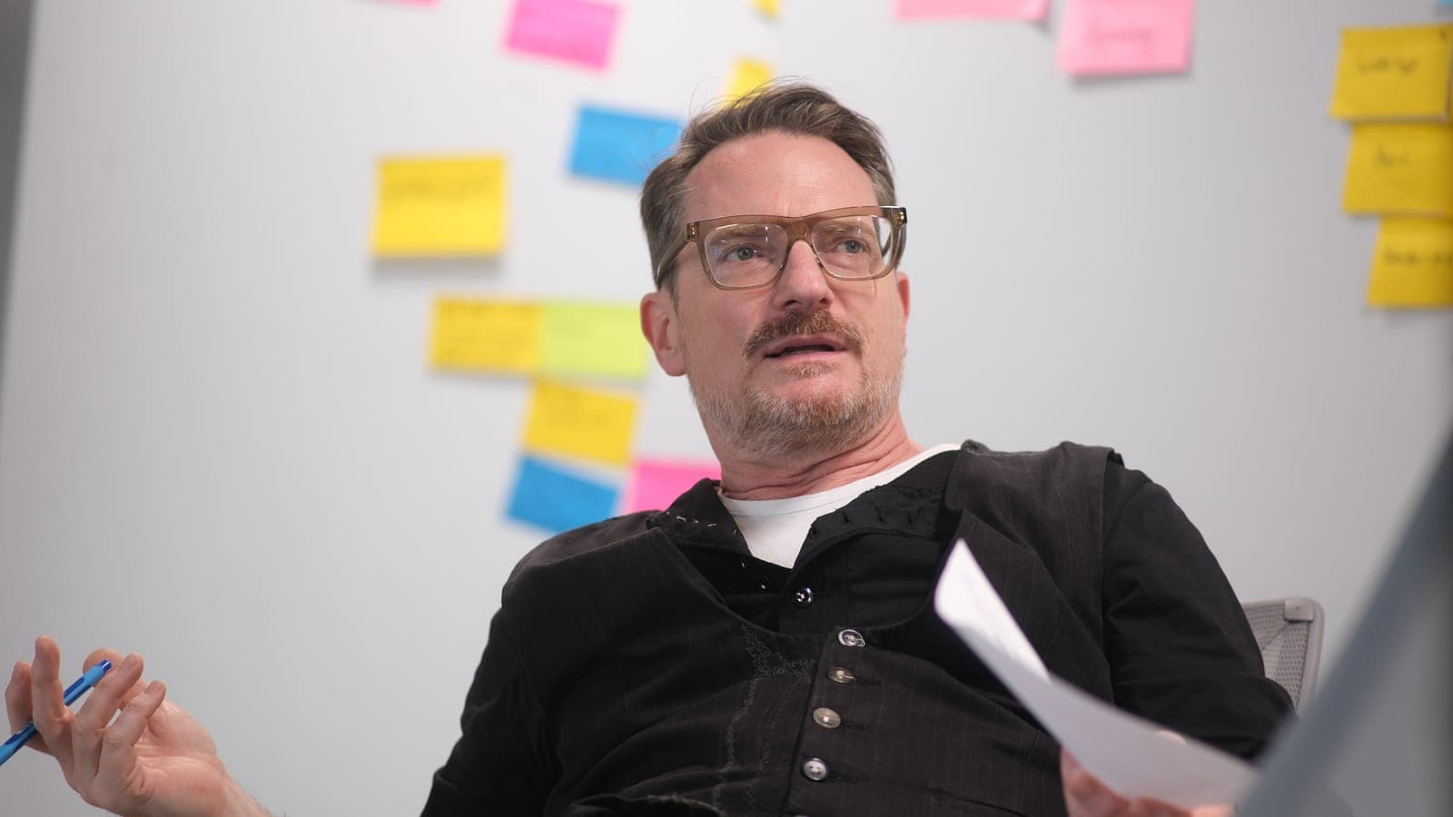 Manuel Kreutz im Gespräch, mit Stift und einem Blatt Papier in den Händen vor einer Wand mit bunten Haftnotizen